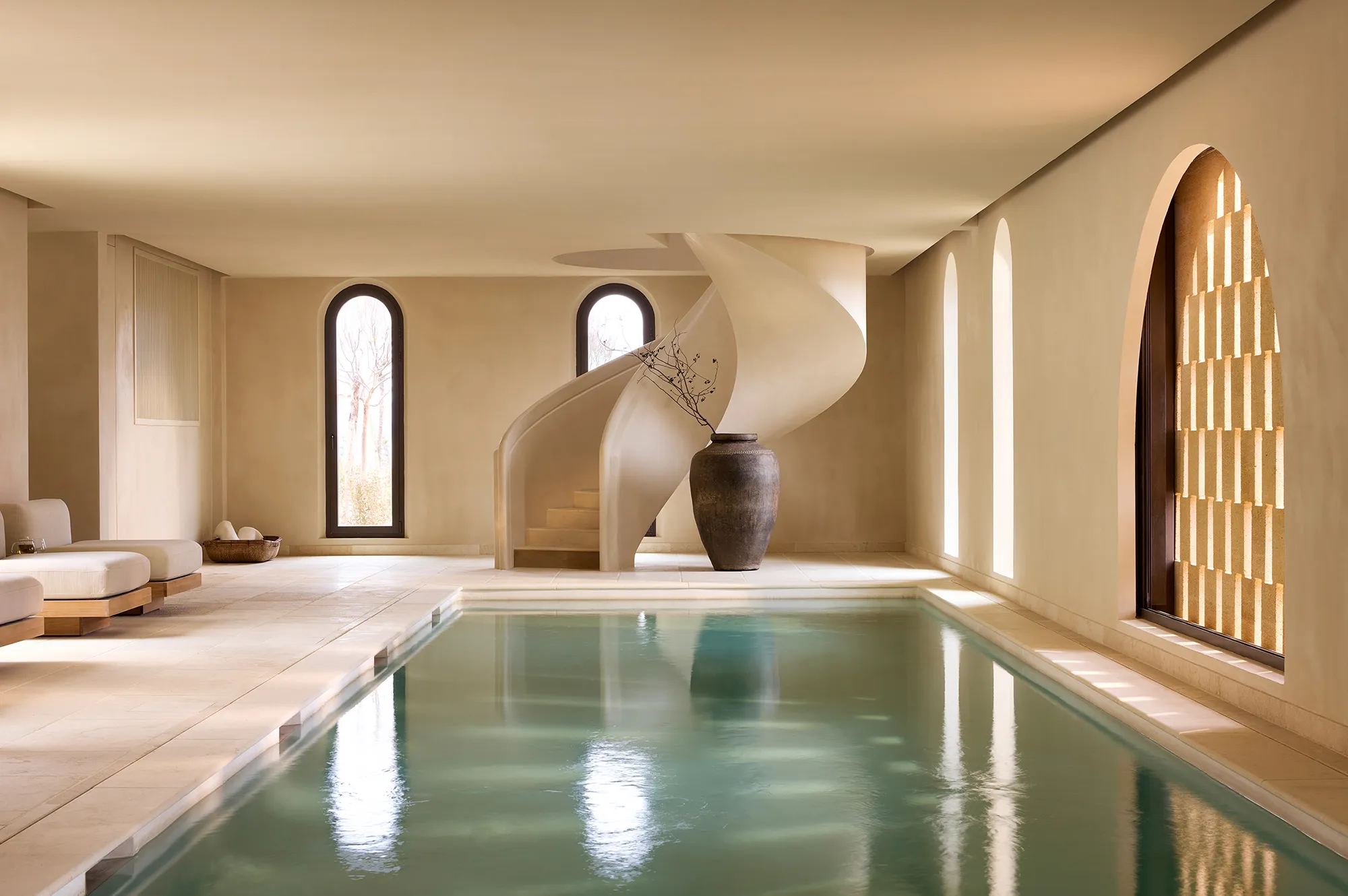 Minimalist indoor pool area with a sculptural spiral staircase and clean lines.