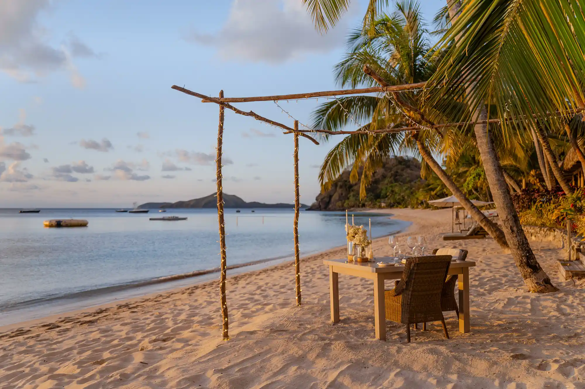 An intimate beachside dining table set under a wooden frame on the white sand of Kokomo Private Island.
