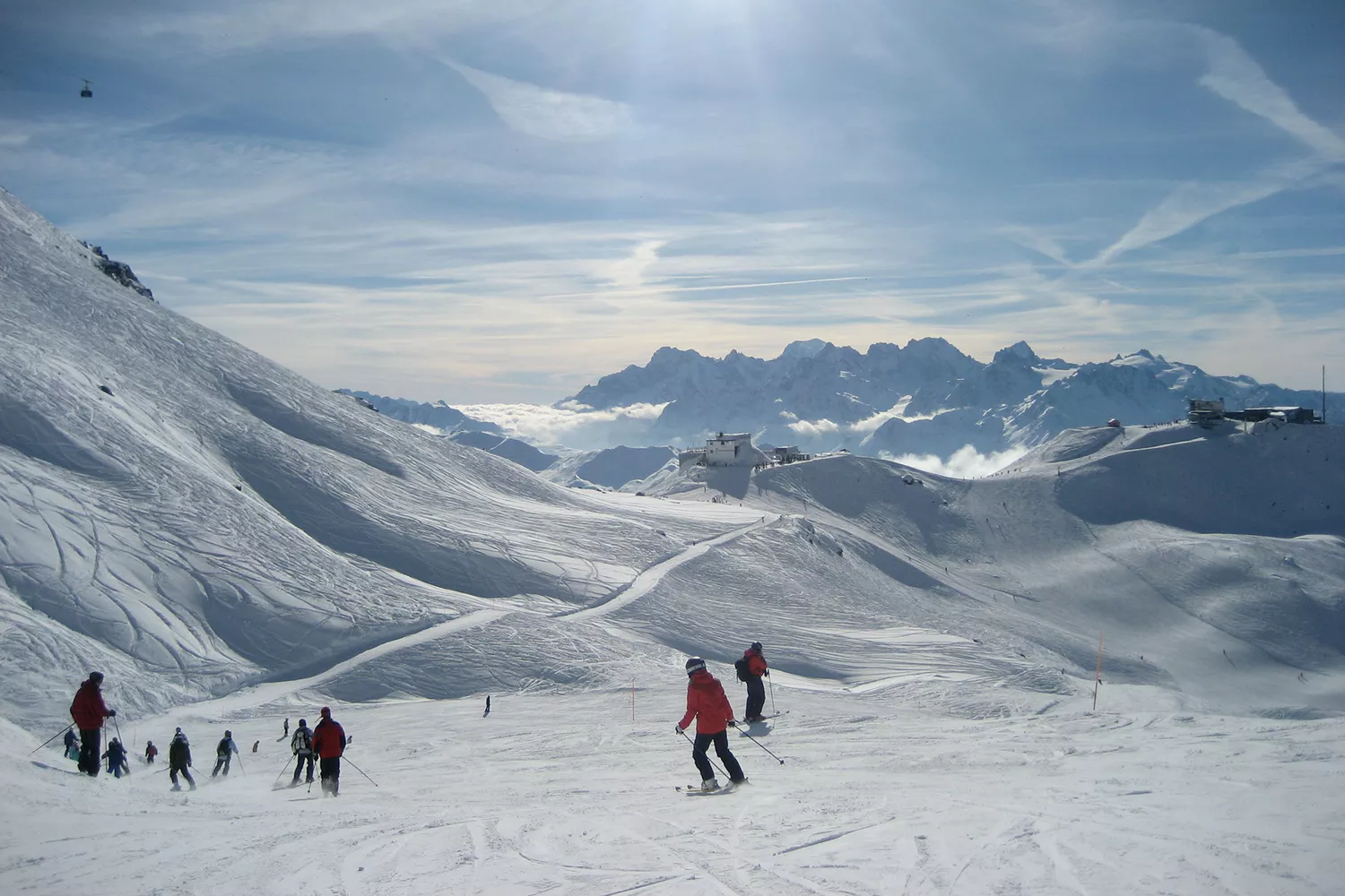 Skiers navigating a groomed slope with the Swiss Alps in the background.