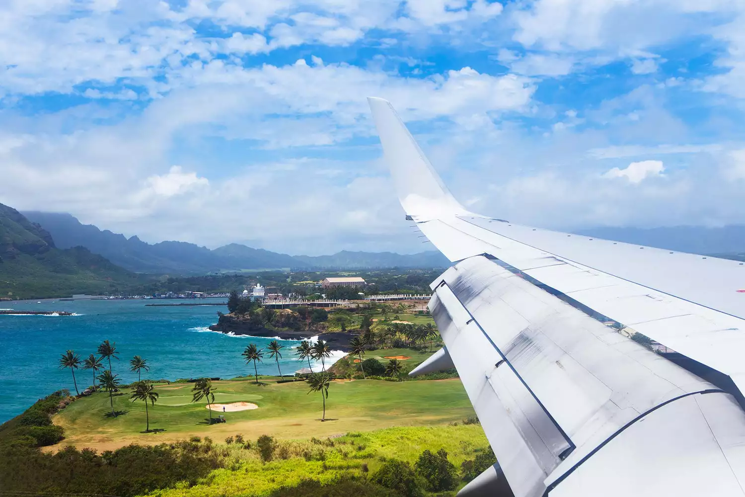 An aerial view of an airplane flying over the lush green coastline of Kauai.