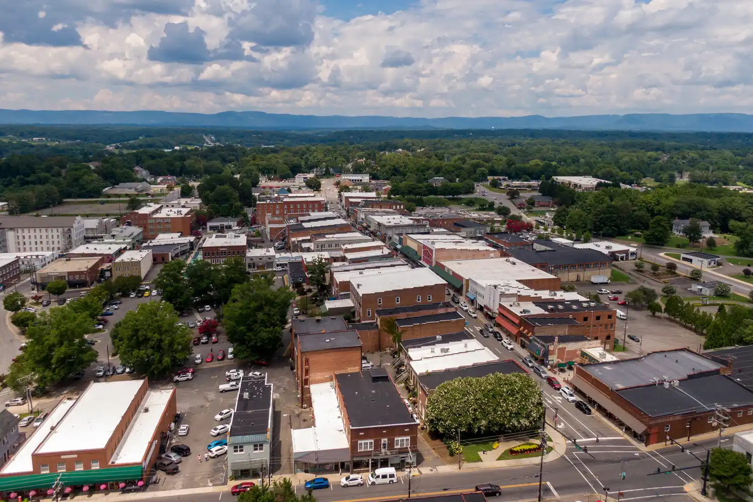 Aerial shot of downtown Mount Airy surrounded by dense green forests and distant mountain peaks.