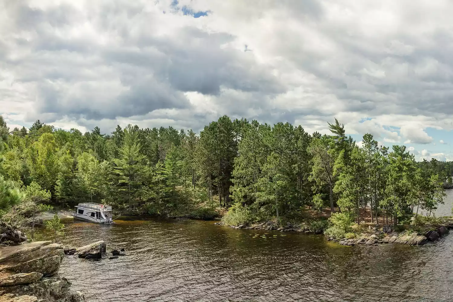 A houseboat floating near the shoreline of a densely wooded island in Voyageurs National Park.