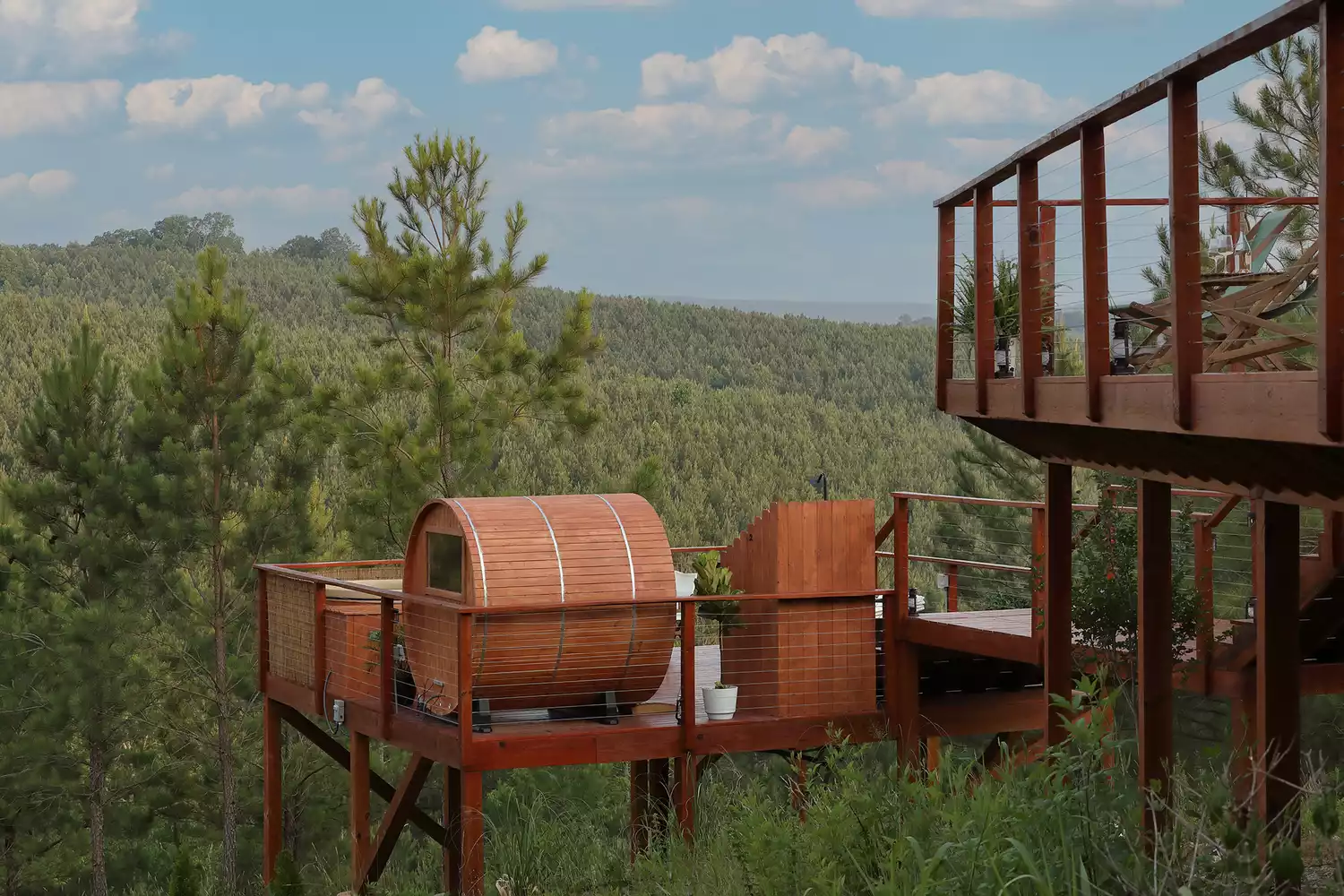 A cedar barrel sauna on a wooden patio overlooking the forest.