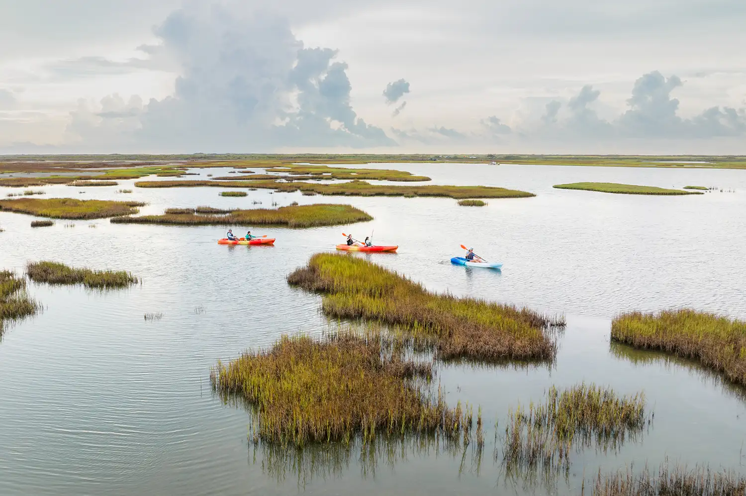 A kayaker paddling through the calm, grassy wetlands of Matagorda