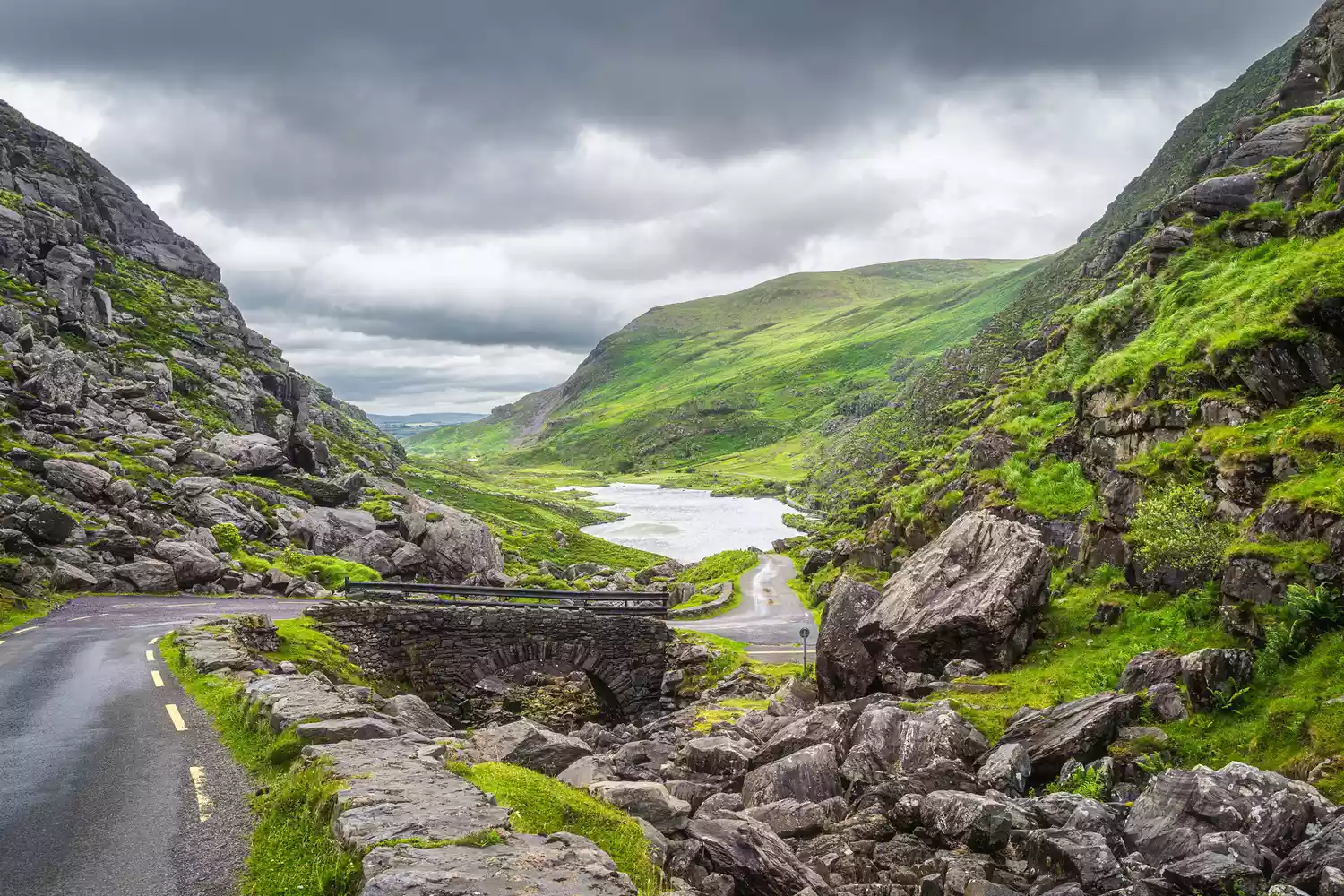A narrow, winding rural road cutting through the lush green mountains of the Iveragh Peninsula.
