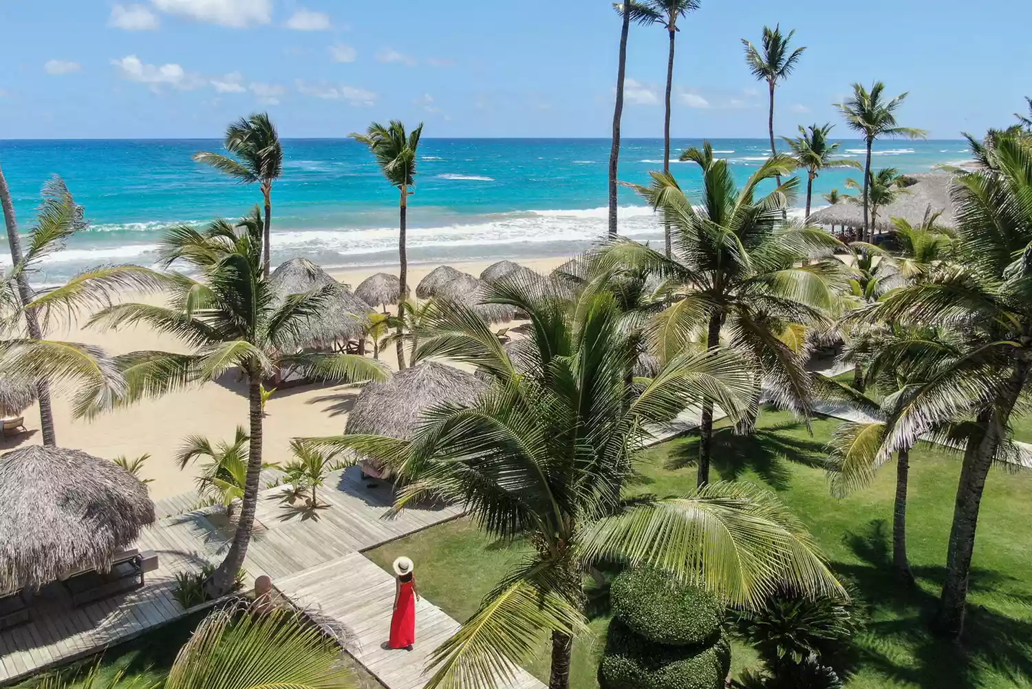 A woman in a red dress walking through the lush tropical grounds of Excellence Punta Cana.