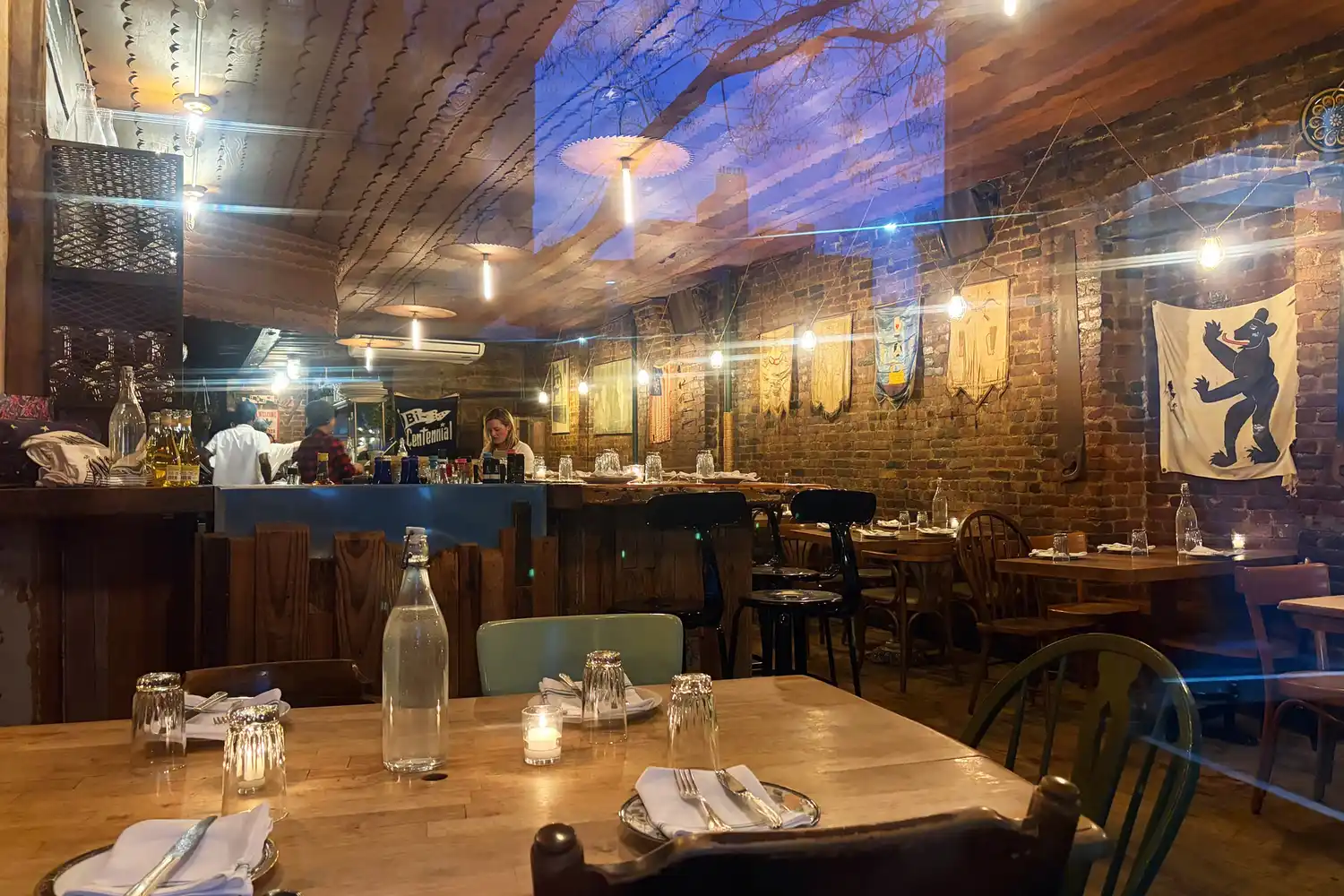 Inside the dining room of St. Anselm restaurant showing wooden furniture and an open kitchen view.