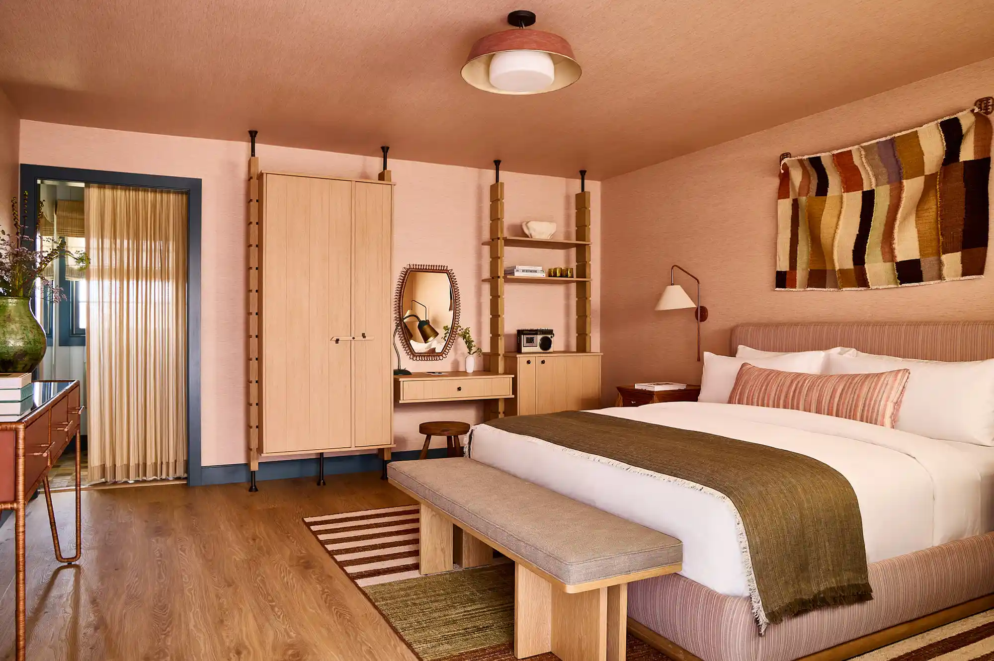 A modern boutique hotel bedroom with a striped wall hanging, wooden bench, and minimalist bed frame.