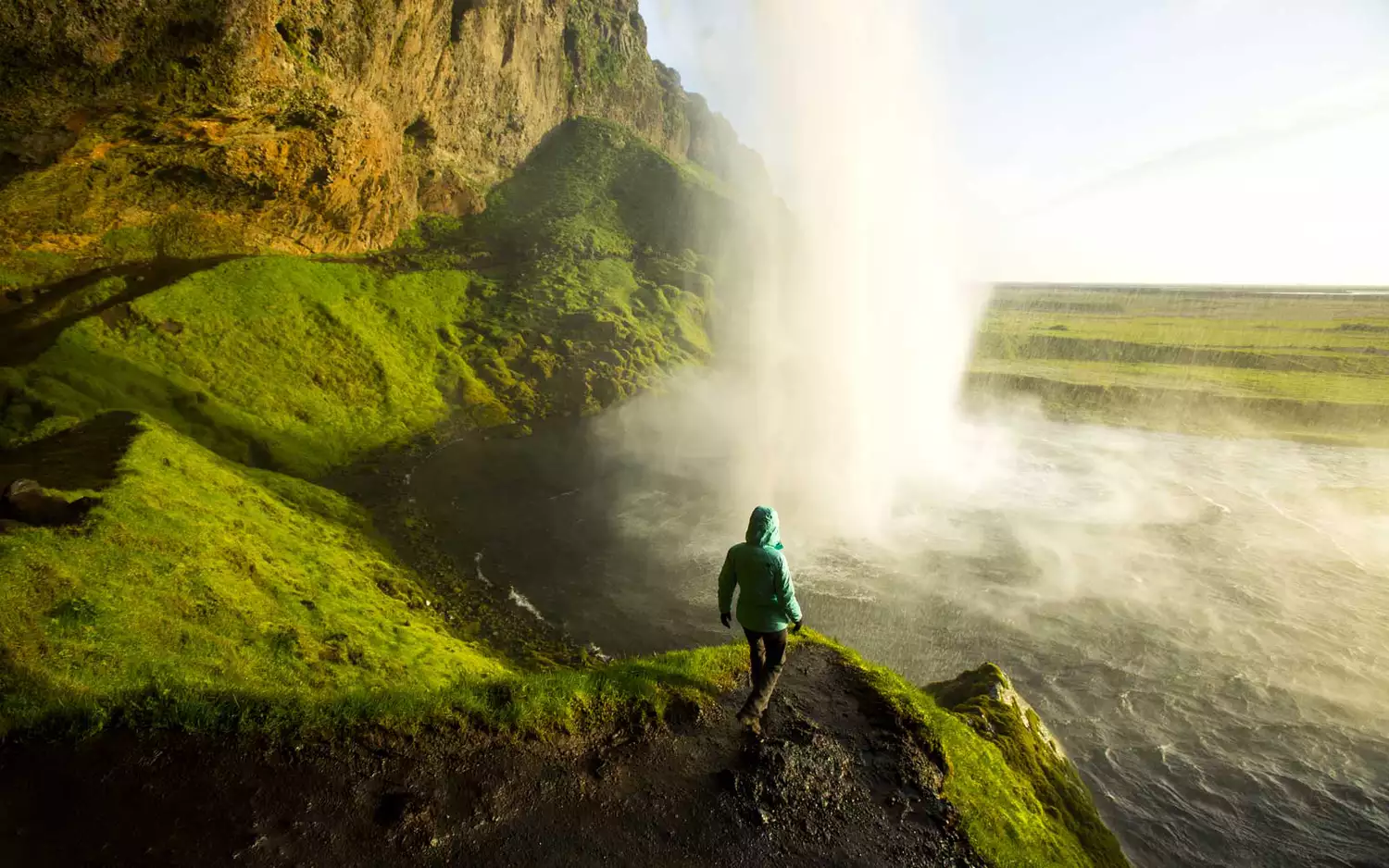 A woman standing behind a large waterfall in Iceland during sunset.