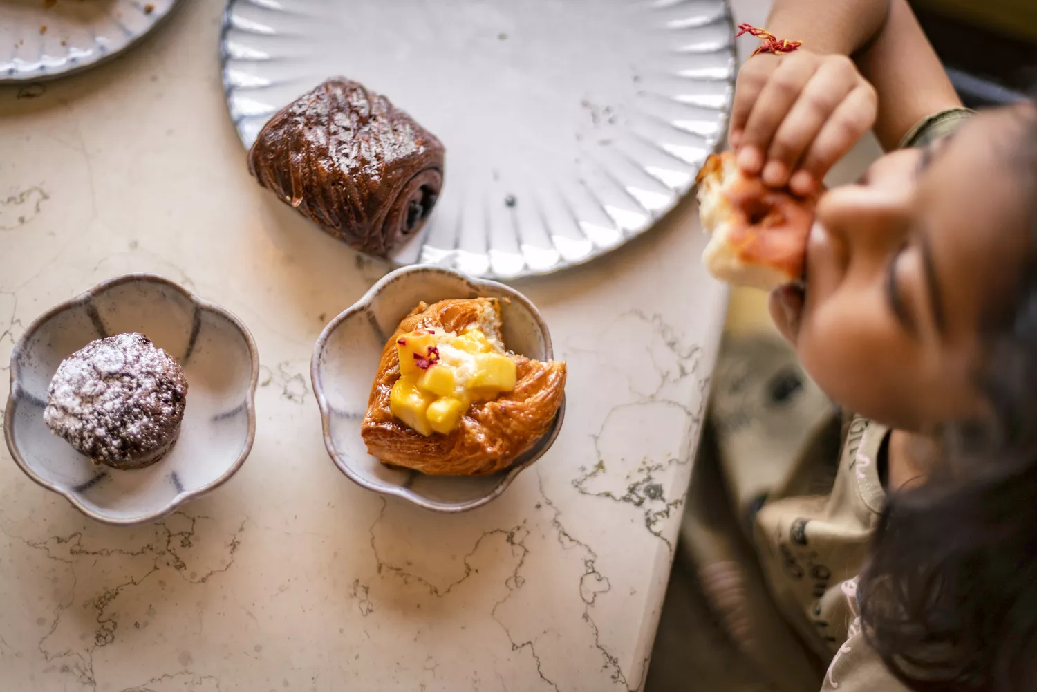 An overhead view of a child eating an assortment of fresh pastries and fruit for breakfast.