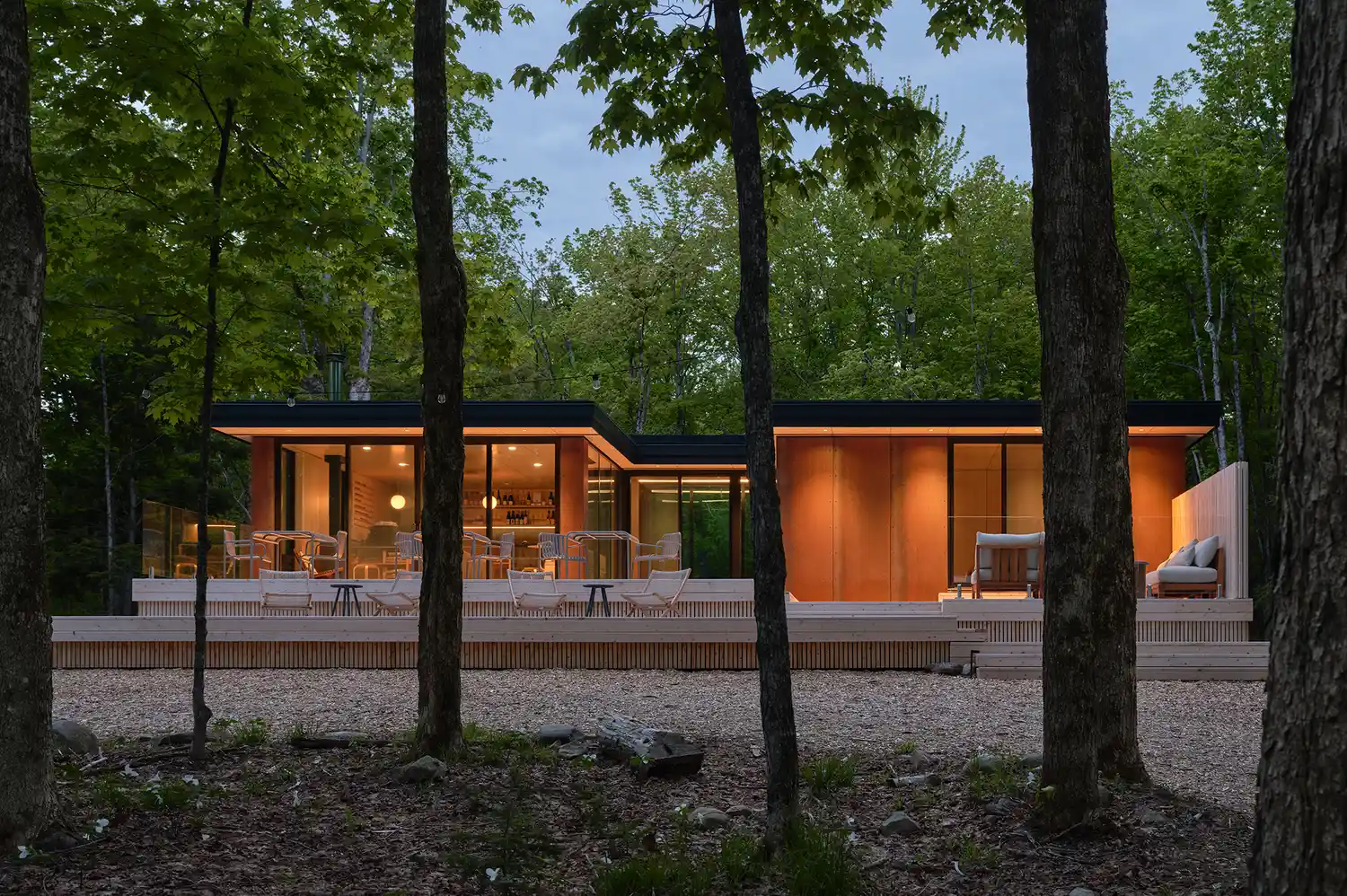 A larger modern structure with wide glass windows located on the forest floor, representing the Hydda building.