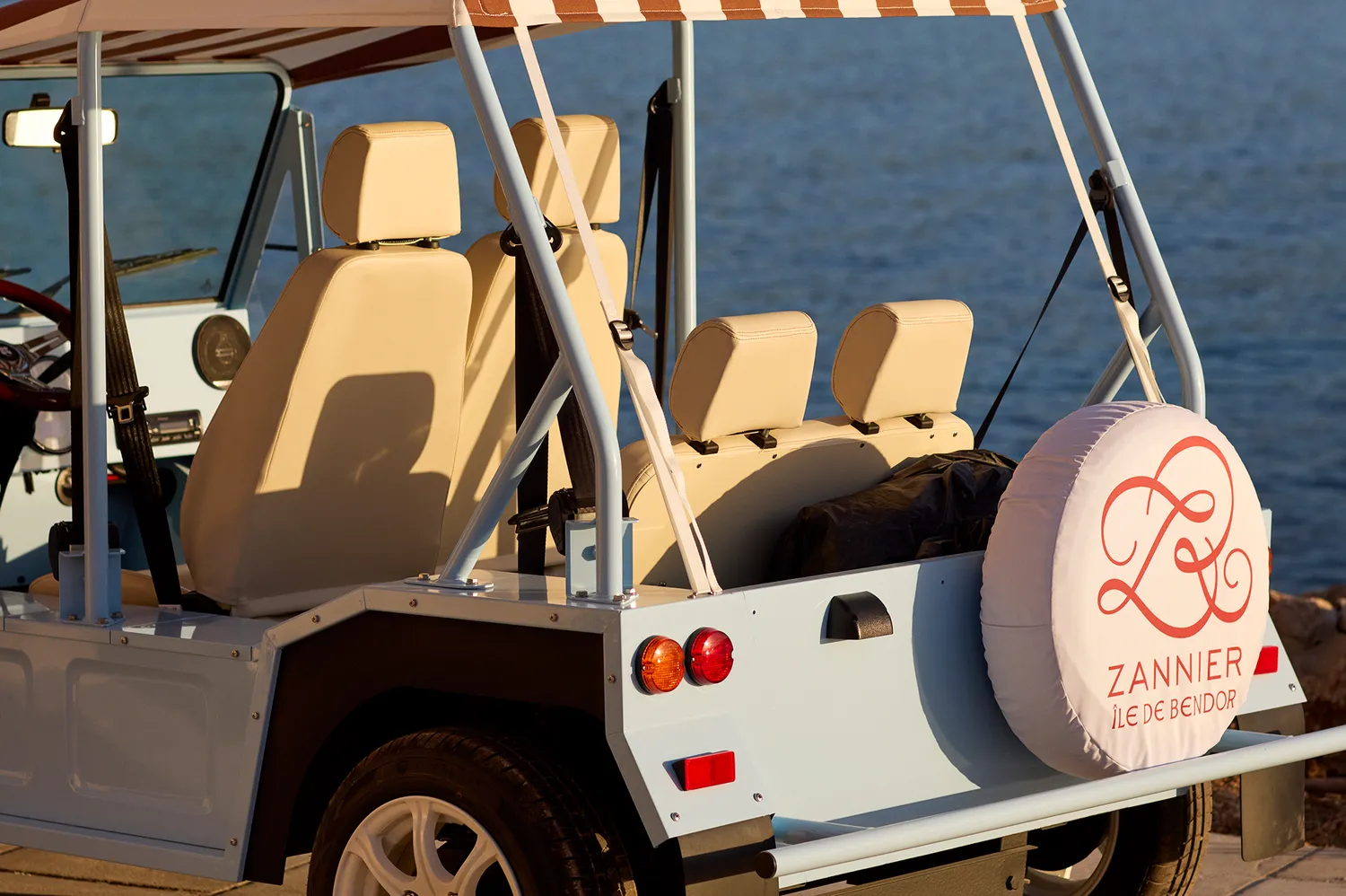A vintage Mini Moke car with the Zannier Île de Bendor logo parked by the water.