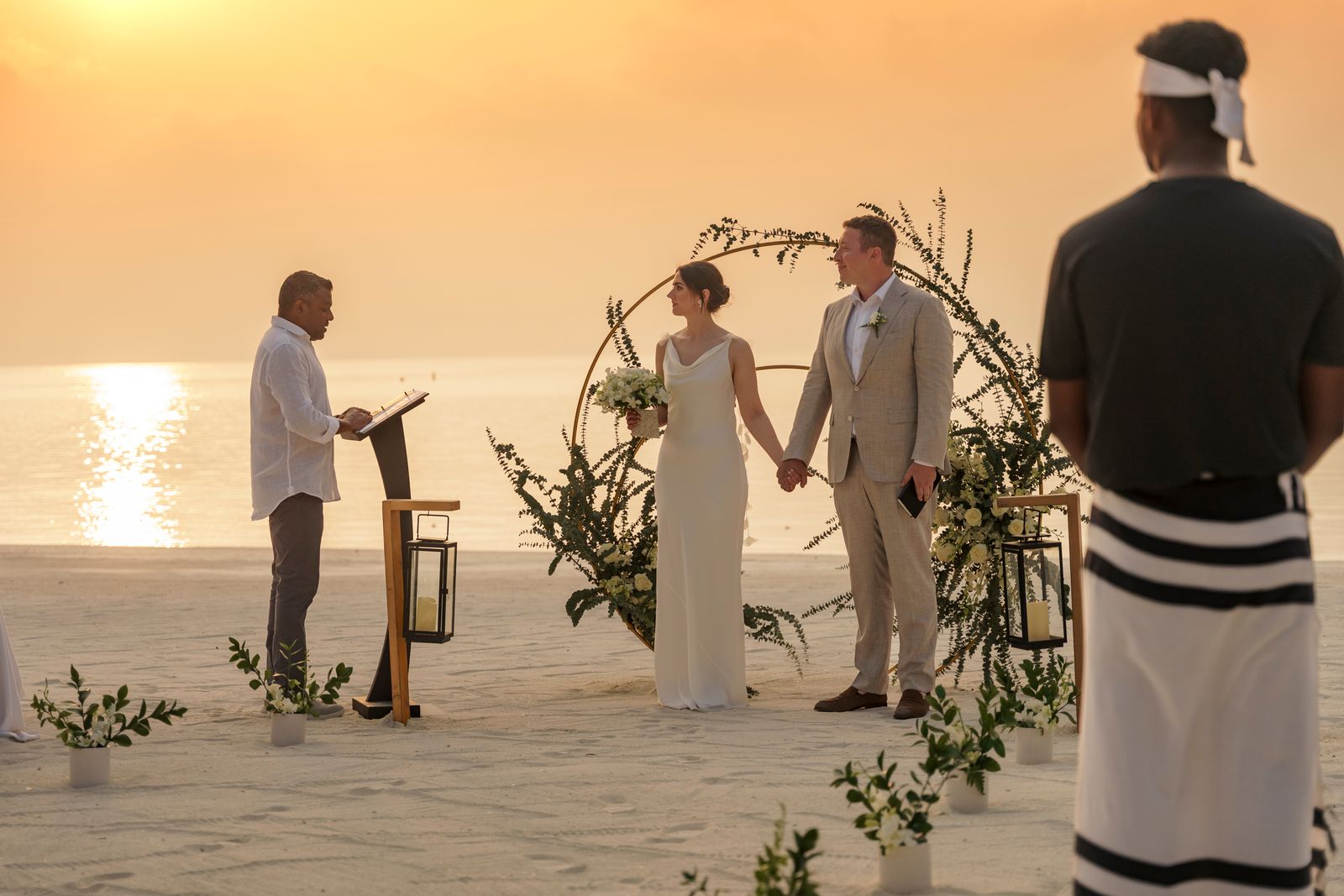 A close-up of a couple in formal wedding attire, including a white dress and a grey suit, holding hands.