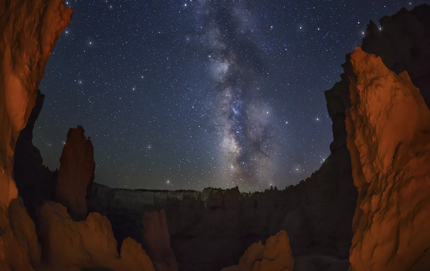 Red rock hoodoo formations in Bryce Canyon National Park silhouetted against a starry night sky.