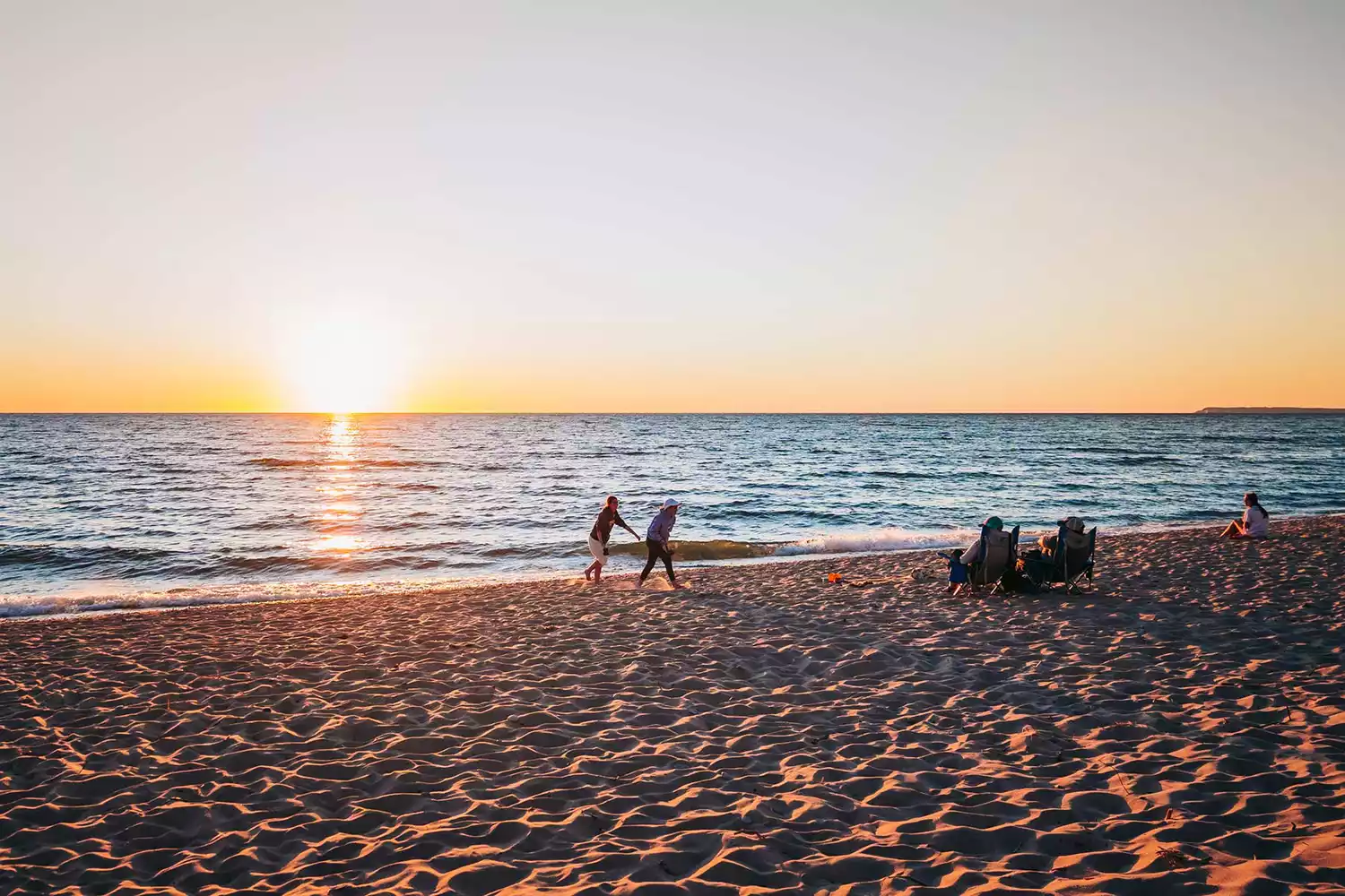 A wide sandy beach at Empire, Michigan with visitors walking near the base of the dunes.