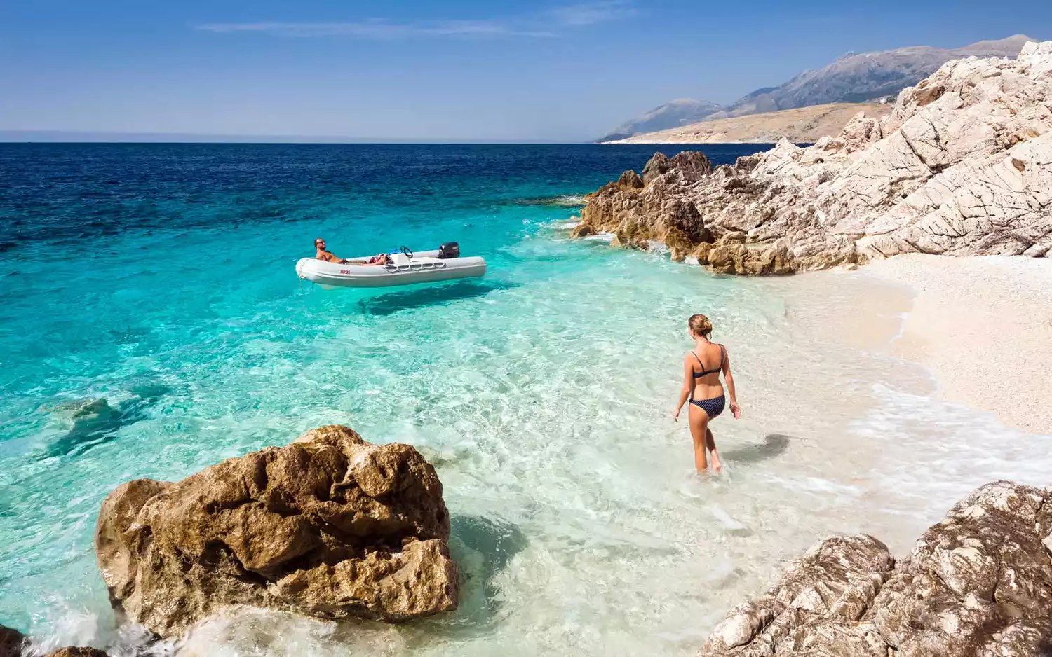 A young woman walking on an Albanian beach near a boat.