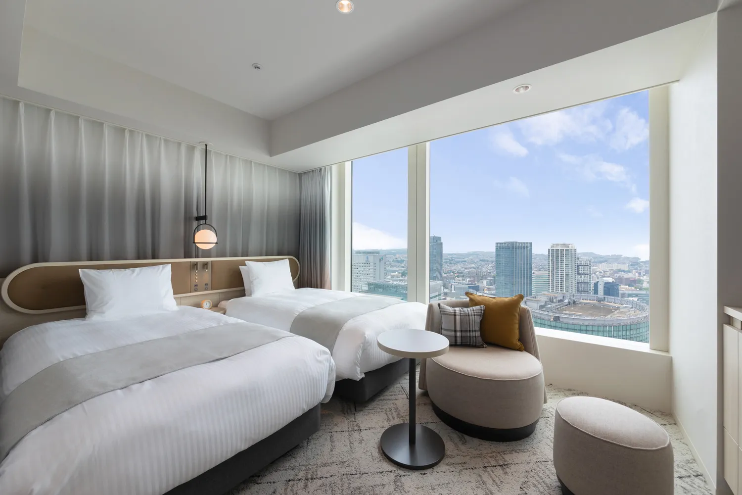A contemporary hotel room with large windows overlooking the Yokohama cityscape.