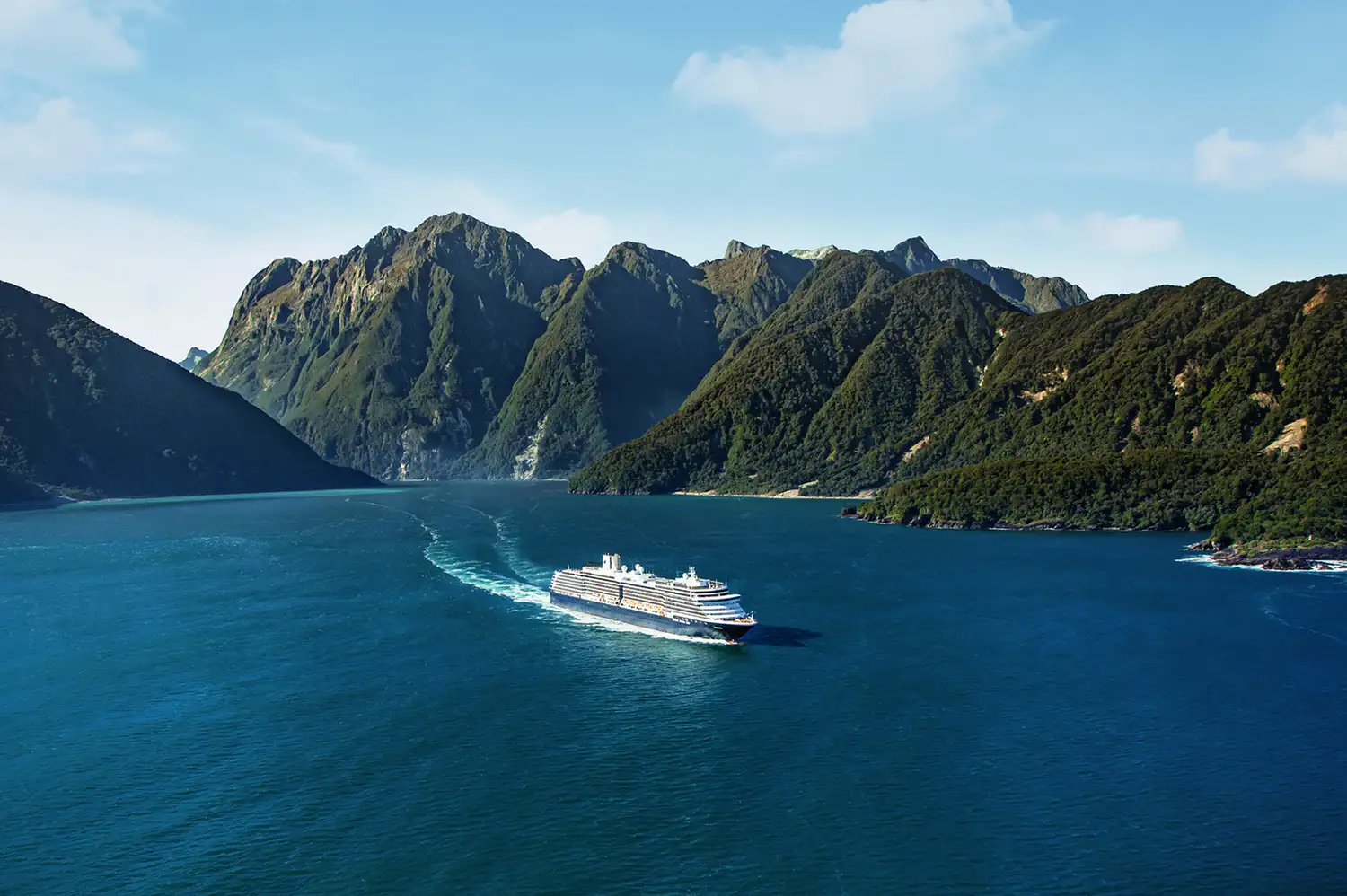 The MS Westerdam ship at the base of towering green cliffs in Milford Sound, New Zealand.