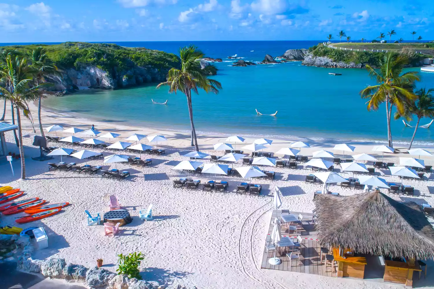 The private beach club area of the Hamilton Princess featuring umbrellas and white sand.