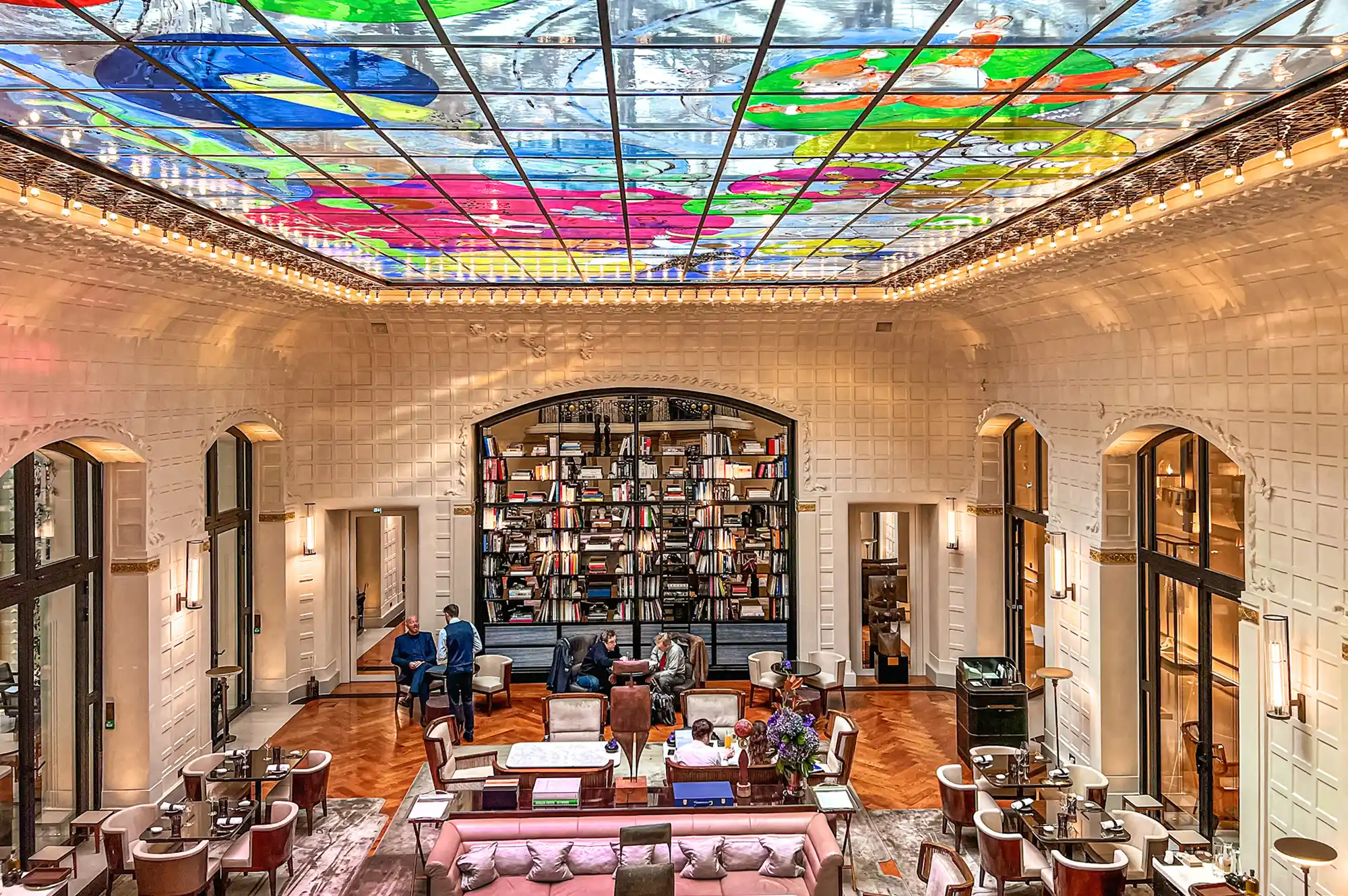 The hotel atrium of Mandarin Oriental Lutetia with a colorful glass ceiling and library-themed decor.