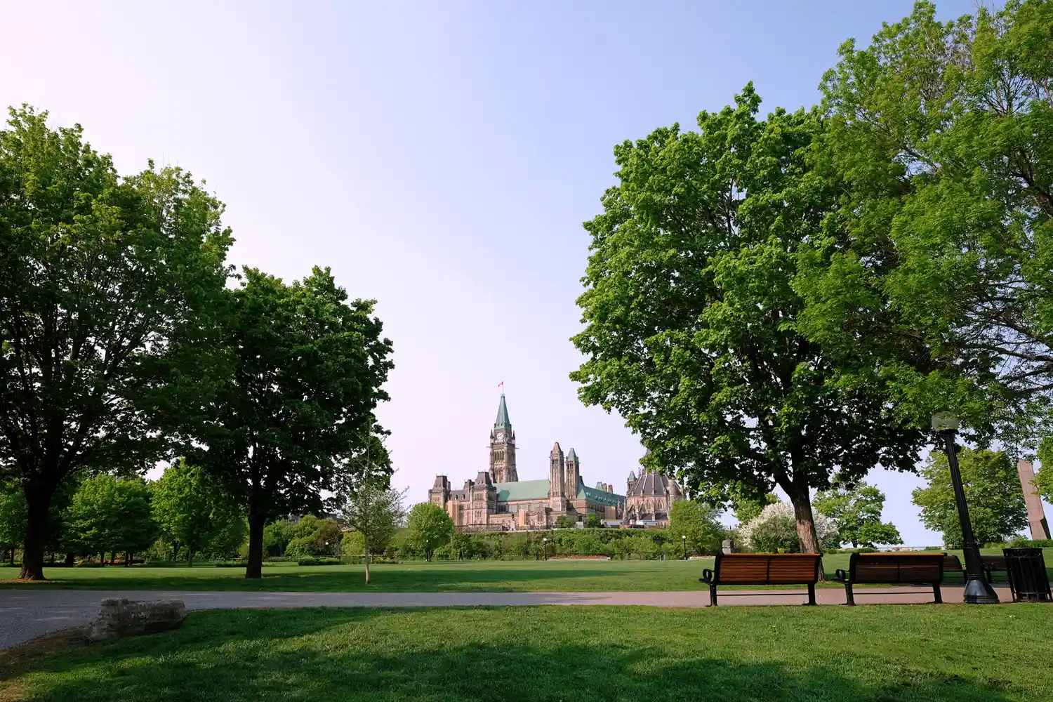A wooden bench in Major's Hill Park overlookng the Gothic-style Parliament of Canada buildings.
