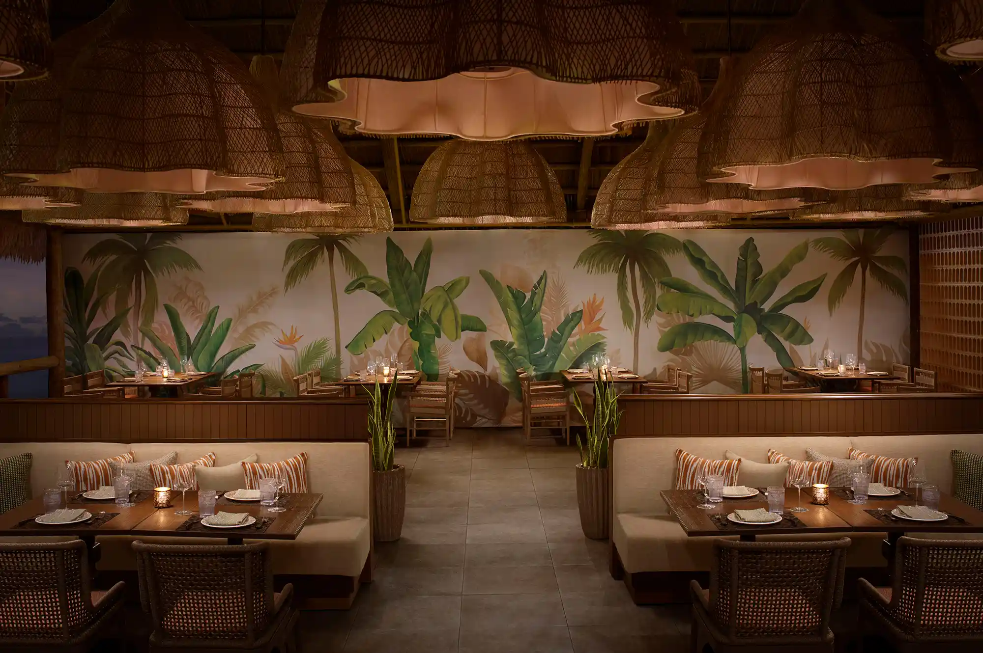 Mediterranean-inspired restaurant interior with wicker light fixtures and tropical wall murals.