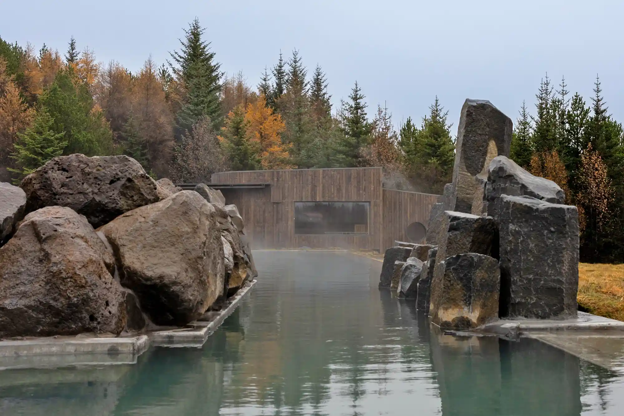 A rock-lined geothermal lagoon pool surrounded by greenery at Laugarás Lagoon.