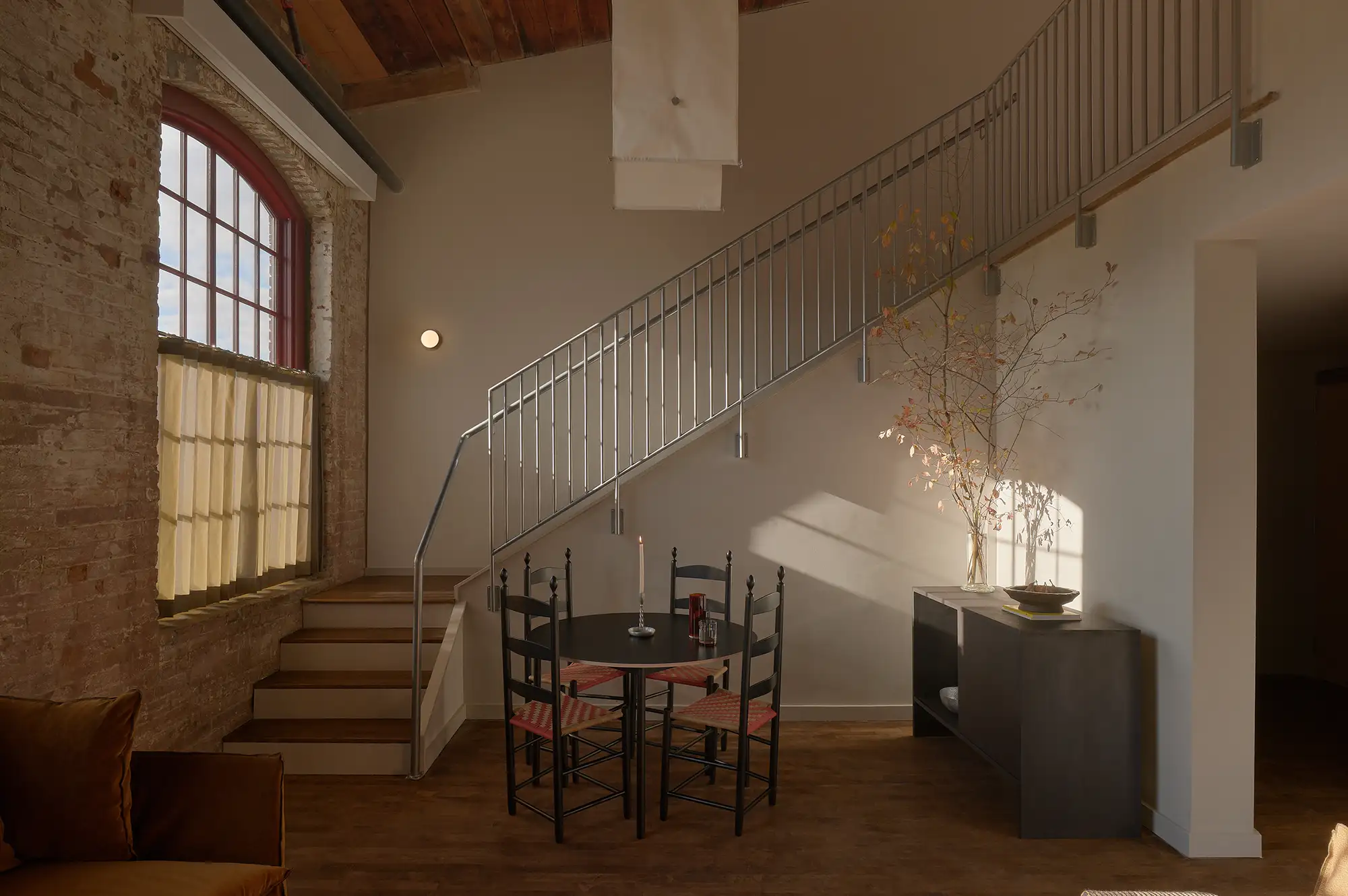 A modern loft suite at Pocketbook Hudson with high arched windows and a mezzanine sleeping area.