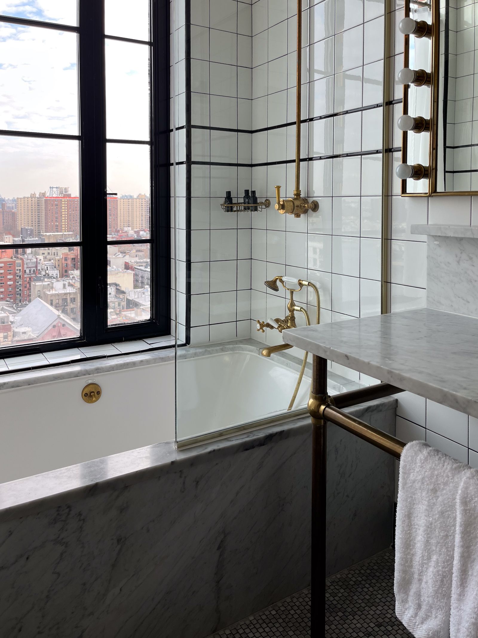A marble mosaic tile bathroom featuring a deep soaking tub by a window with city views.