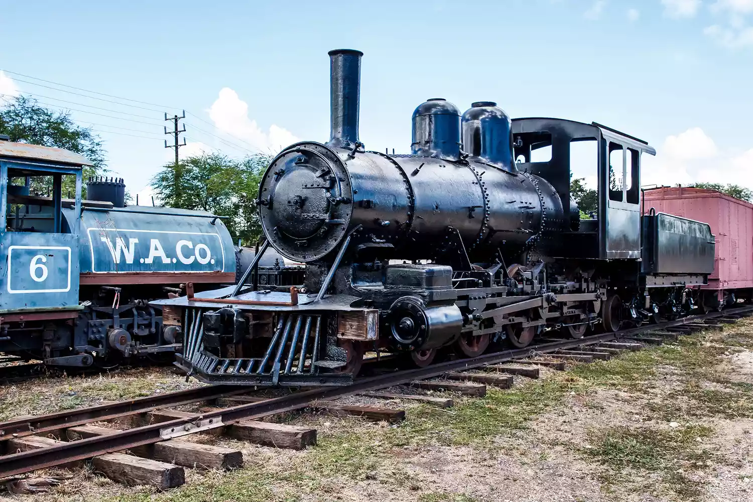 Black and blue vintage steam engines parked at the Ewa railroad yard.