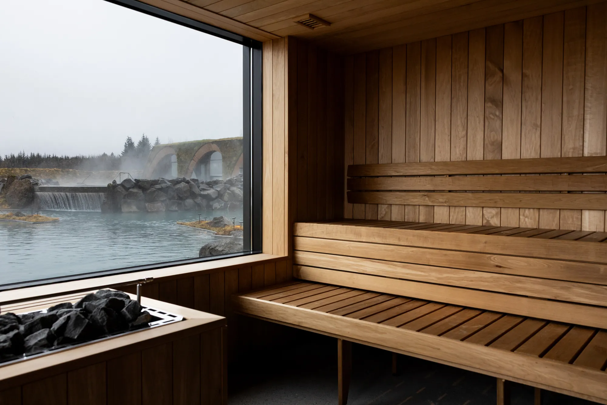 Interior view of a wooden sauna at Laugarás Lagoon with a large window overlooking the lagoon and waterfall.